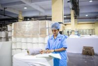 Seorang operator produksi sedang melakukan pemeriksaan kualitas produk dengan cermat di sepanjang garis perakitan pabrik manufaktur modern.