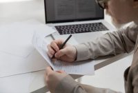 Tampilan berkas lamaran kerja berformat sederhana yang diletakkan di samping laptop saat proses evaluasi kualifikasi rekrutmen.