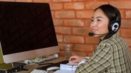 Seorang petugas layanan pelanggan alih daya sedang menangani komunikasi dengan konsumen menggunakan peranti dengar di kantor, menunjukkan profesionalisme serta fokus tinggi dalam menyelesaikan setiap kendala pengguna.