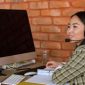 Seorang petugas layanan pelanggan alih daya sedang menangani komunikasi dengan konsumen menggunakan peranti dengar di kantor, menunjukkan profesionalisme serta fokus tinggi dalam menyelesaikan setiap kendala pengguna.
