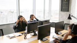 Seorang agen pusat layanan alih daya sedang mendengarkan keluhan pelanggan dengan cermat sembari mencatat data pada sistem komputer kantor.