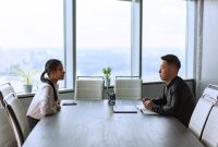 Dua manajer sumber daya manusia sedang mengevaluasi berkas lamaran kerja calon karyawan dalam sesi wawancara di kantor.