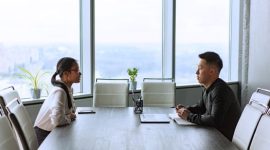 Dua manajer sumber daya manusia sedang mengevaluasi berkas lamaran kerja calon karyawan dalam sesi wawancara di kantor.