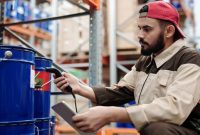 Para pekerja alih daya sedang melakukan pemindaian data barang menggunakan perangkat cerdas di sebuah gudang logistik modern untuk memastikan ketepatan dan kecepatan pengiriman paket konsumen.