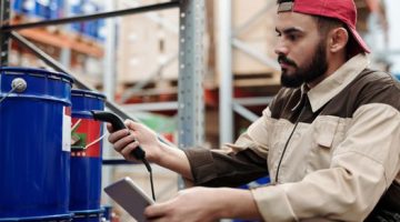 Para pekerja alih daya sedang melakukan pemindaian data barang menggunakan perangkat cerdas di sebuah gudang logistik modern untuk memastikan ketepatan dan kecepatan pengiriman paket konsumen.