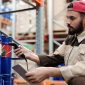 Para pekerja alih daya sedang melakukan pemindaian data barang menggunakan perangkat cerdas di sebuah gudang logistik modern untuk memastikan ketepatan dan kecepatan pengiriman paket konsumen.
