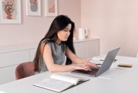 Seorang profesional muda melakukan sesi wawancara kerja online dengan pencahayaan terang dan gestur tubuh yang percaya diri di depan laptop. Penataan sudut kamera yang sejajar dengan mata membantu menciptakan kesan komunikasi yang hangat dan meyakinkan perekrut.